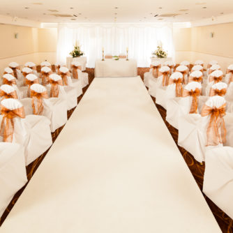 The Parkside Suite at Mercure Tunbridge Wells Hotel ready for a wedding ceremony, white aisle, peach ribbon, candles, flowers